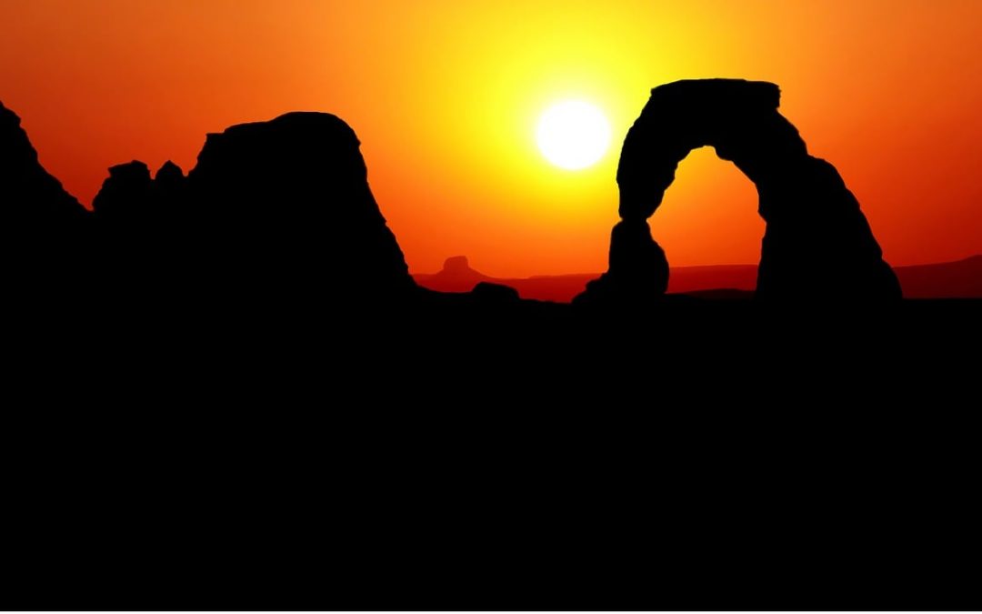 Silhouette of Delicate Arch at sunset in Arches National Park, with a glowing orange sky and the sun setting behind the arch.