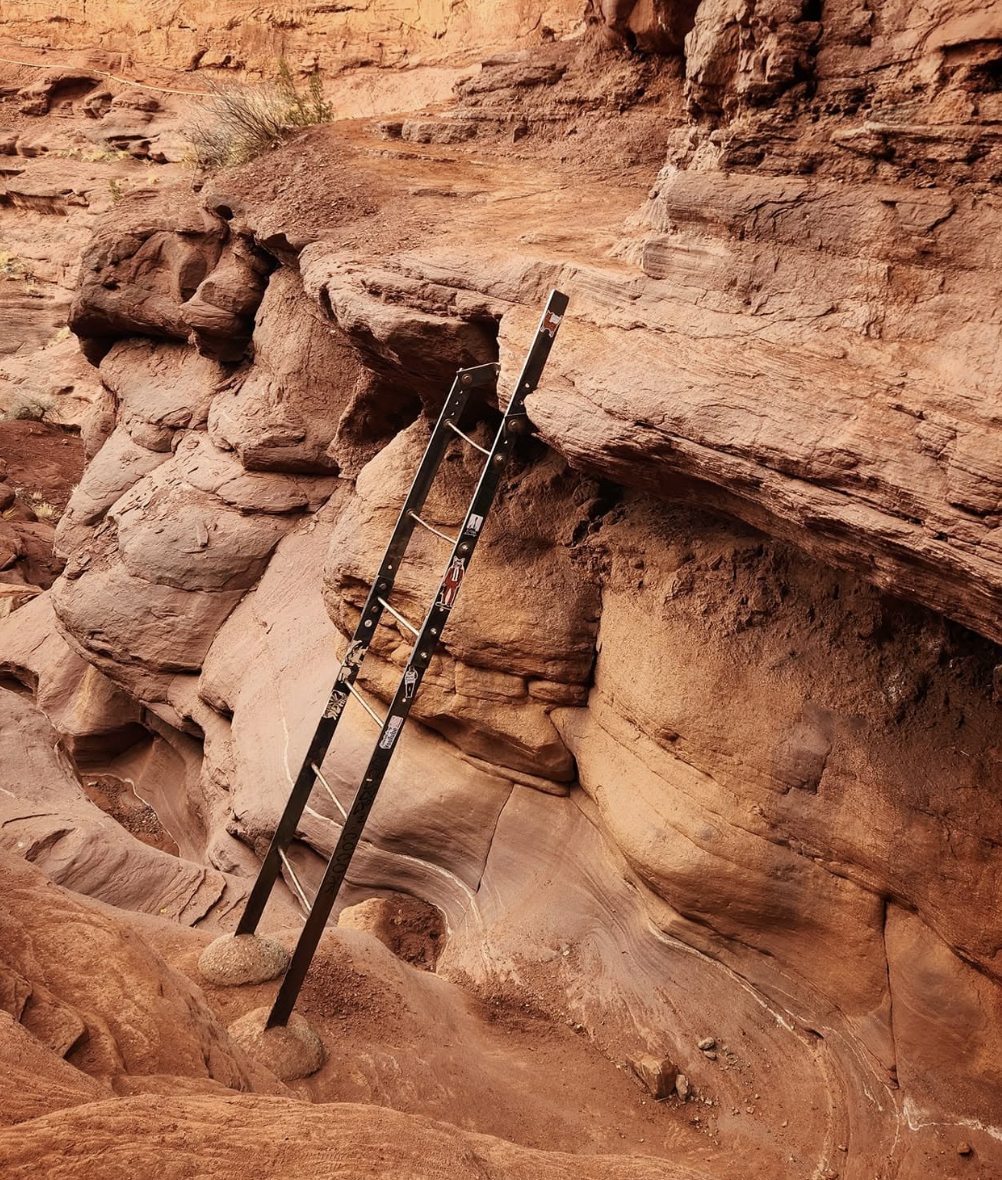 The short metal ladder on the Fisher Towers trail descending a rock step, with a bolted handhold beside it